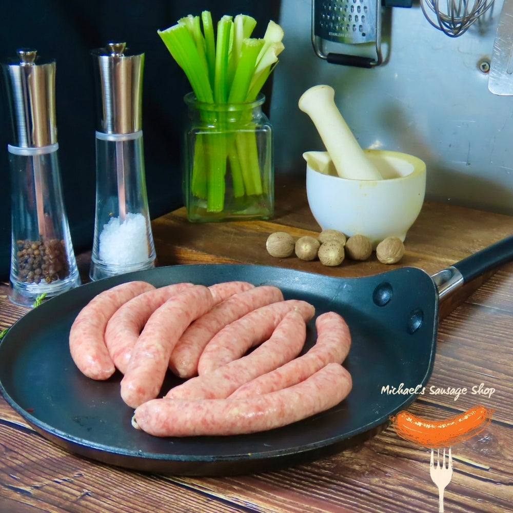 Raw small chippolata sausages on a pan with kitchen items in the background. By Michael's Sausage Shop.