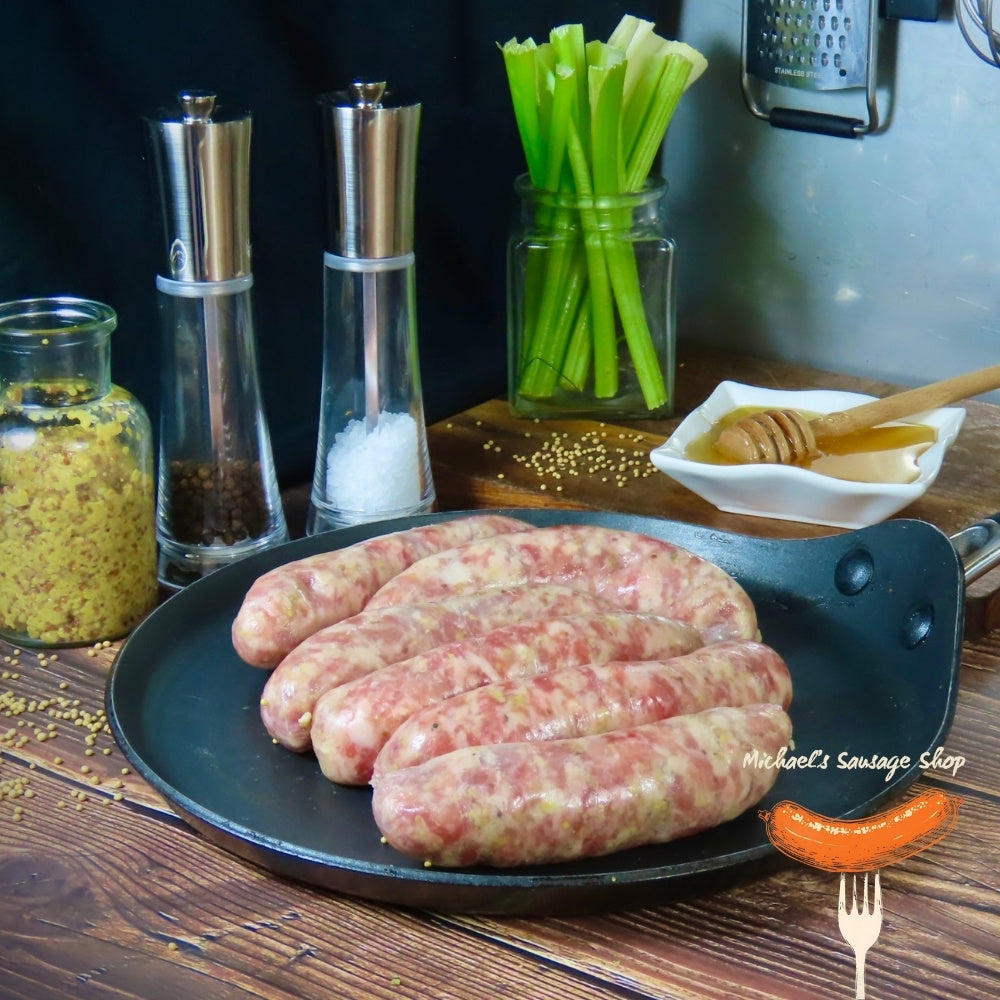 Raw Honey & Mustard sausages on a pan with seasonings and vegetables in the background. By Michael's Sausage Shop.
