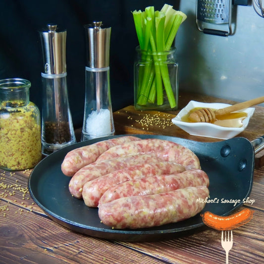 Raw Honey & Mustard sausages on a pan with seasonings and vegetables in the background. By Michael's Sausage Shop.