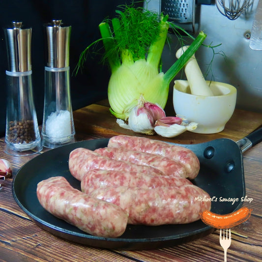 Raw Italian Fennel and Garlic sausages on a pan with fennel, garlic, and kitchen utensils in the background. By Michael's Sausage Shop.