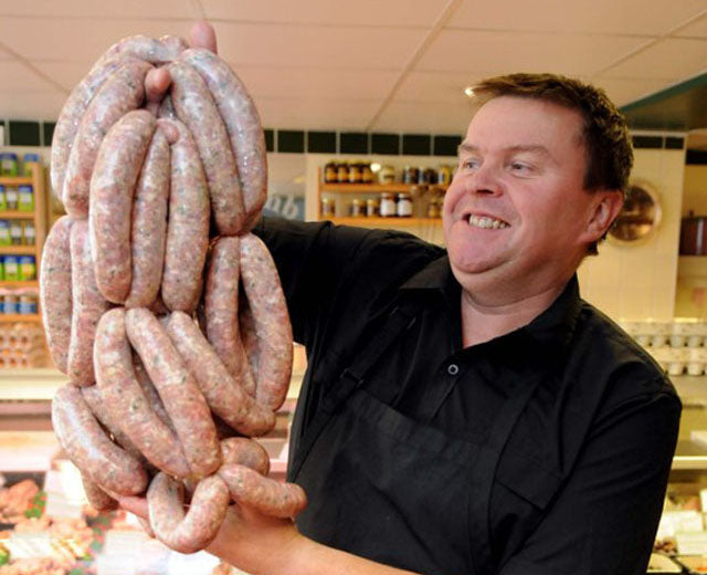 Michael from Michael's Sausage Shop holding a large bundle of raw sausages in a store setting.