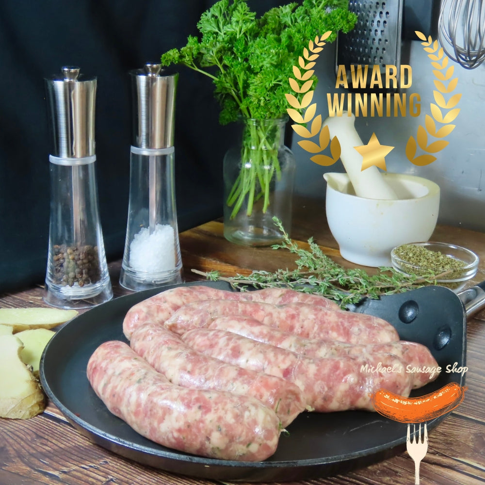 Uncooked Malmesbury King sausages on a pan with herbs, salt and pepper shakers, by Michael's Sausage Shop.